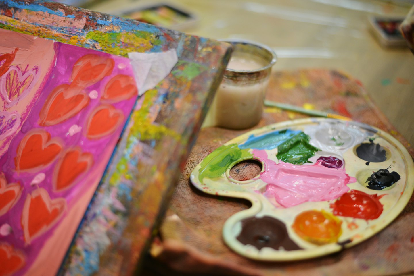 Painter's palette with colorful paint rests beside a heart painting.