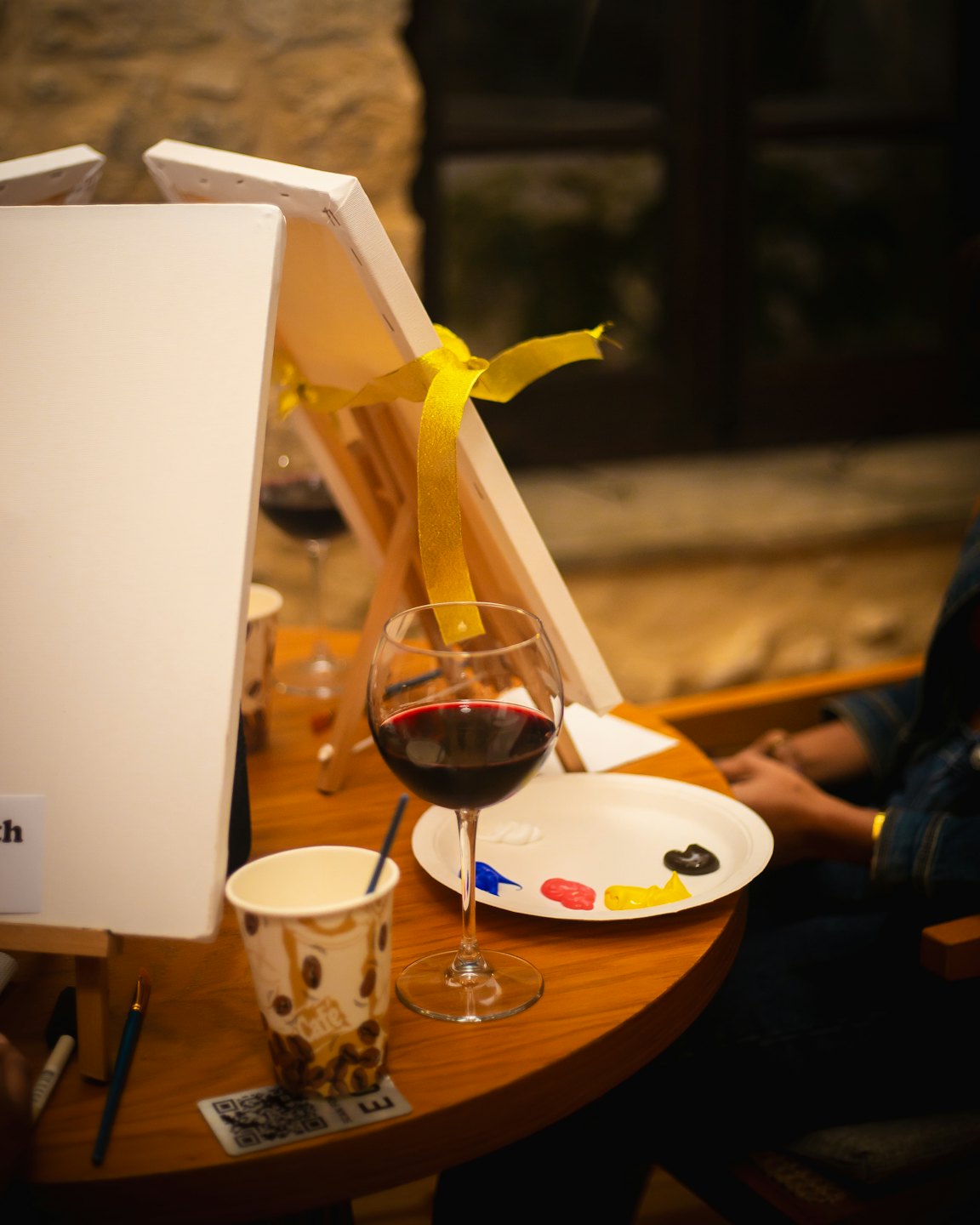Paintbrushes and a palette rest on a table beside wine glasses.