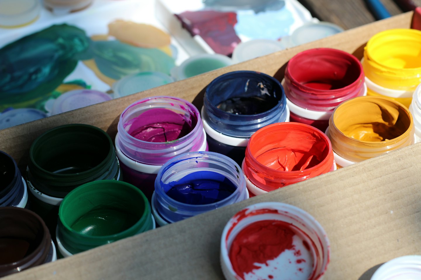 Open jars of colorful paints in a cardboard box.