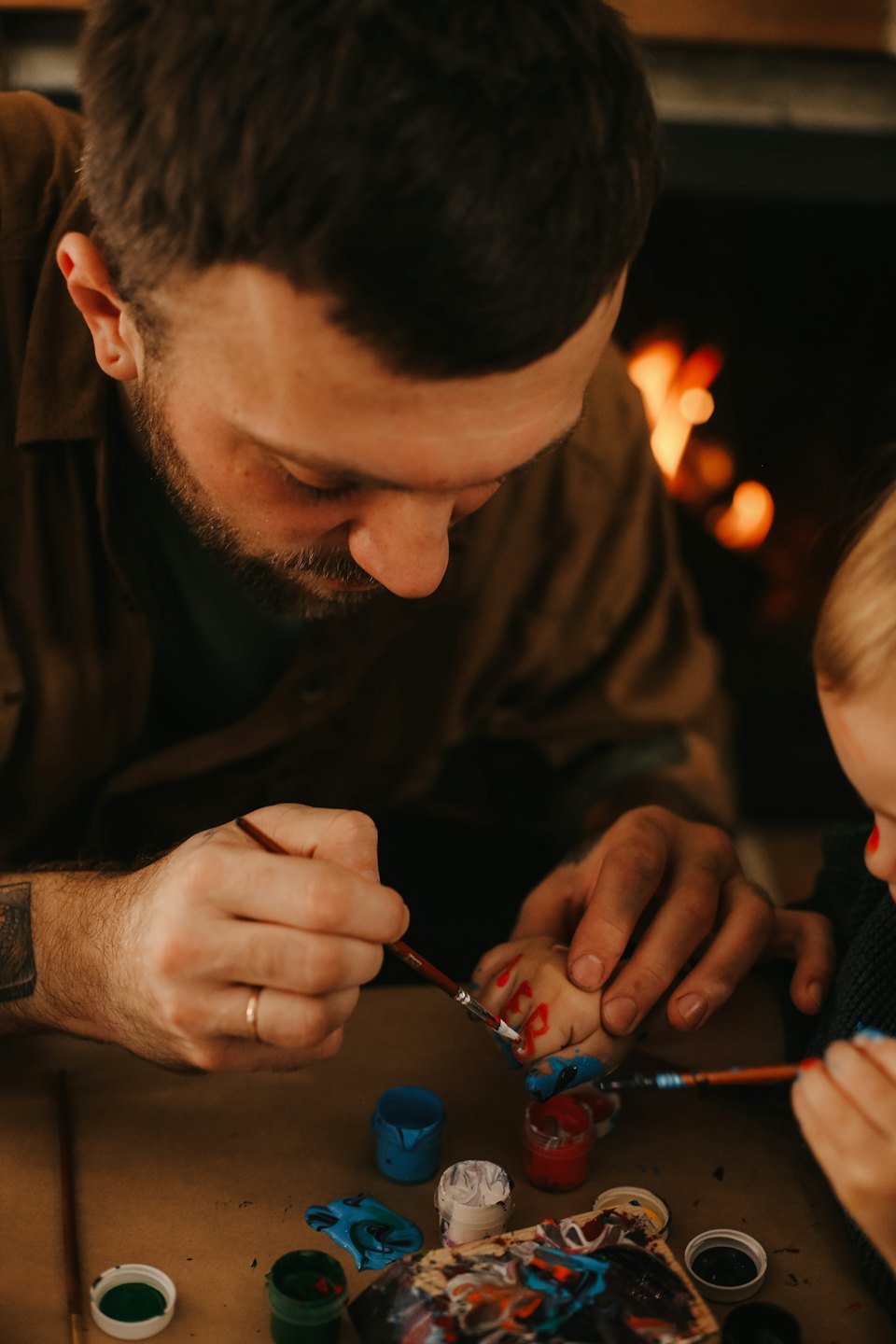 An adult paints red designs on a child's hand.