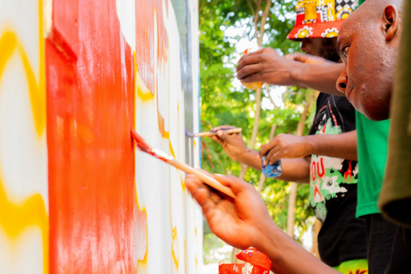 People painting a mural with red and yellow paint.