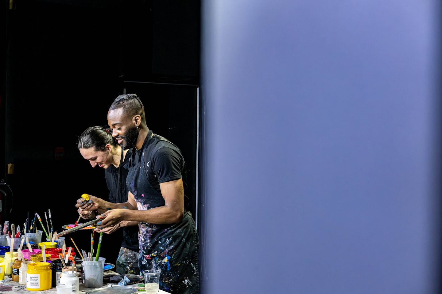 Two artists mixing paint on palettes in their studio.